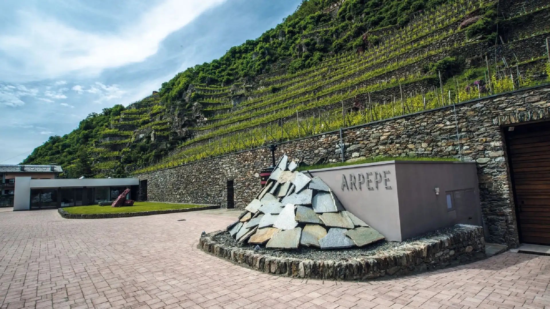 Arpepe’s winery at the foot of its terraced Valtellina vineyards, combining modern architecture with historic stone-built slopes.
