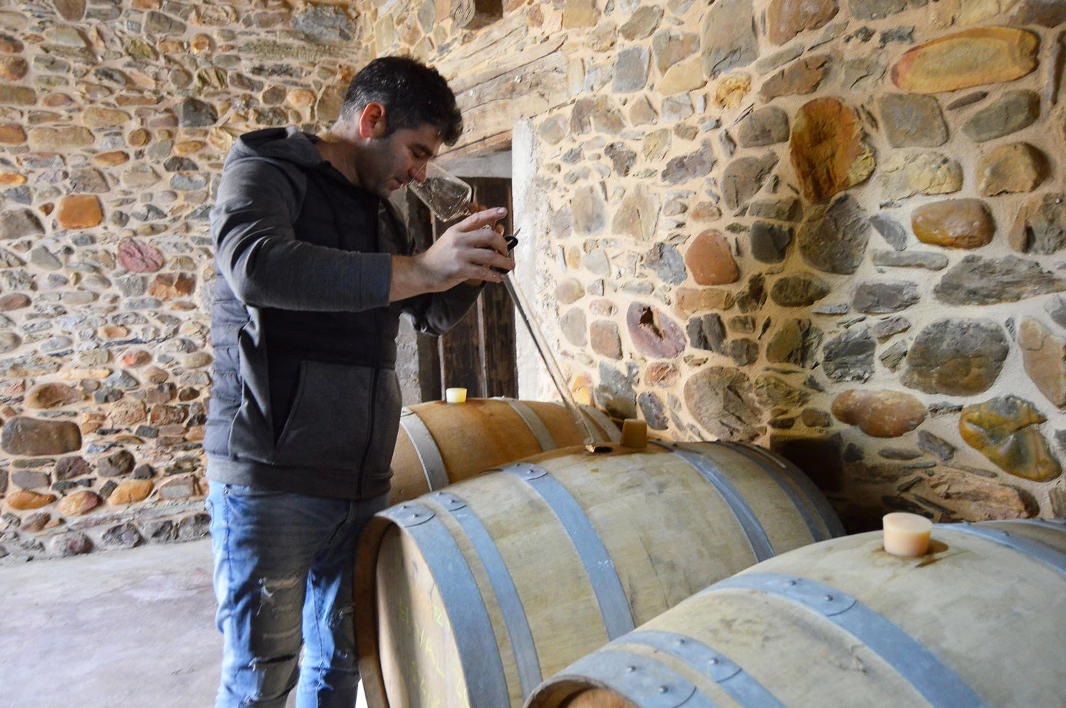 Spanish producer César Márquez sampling wine from barrels in a rustic stone winery, showcasing the winemaking process in Bierzo.