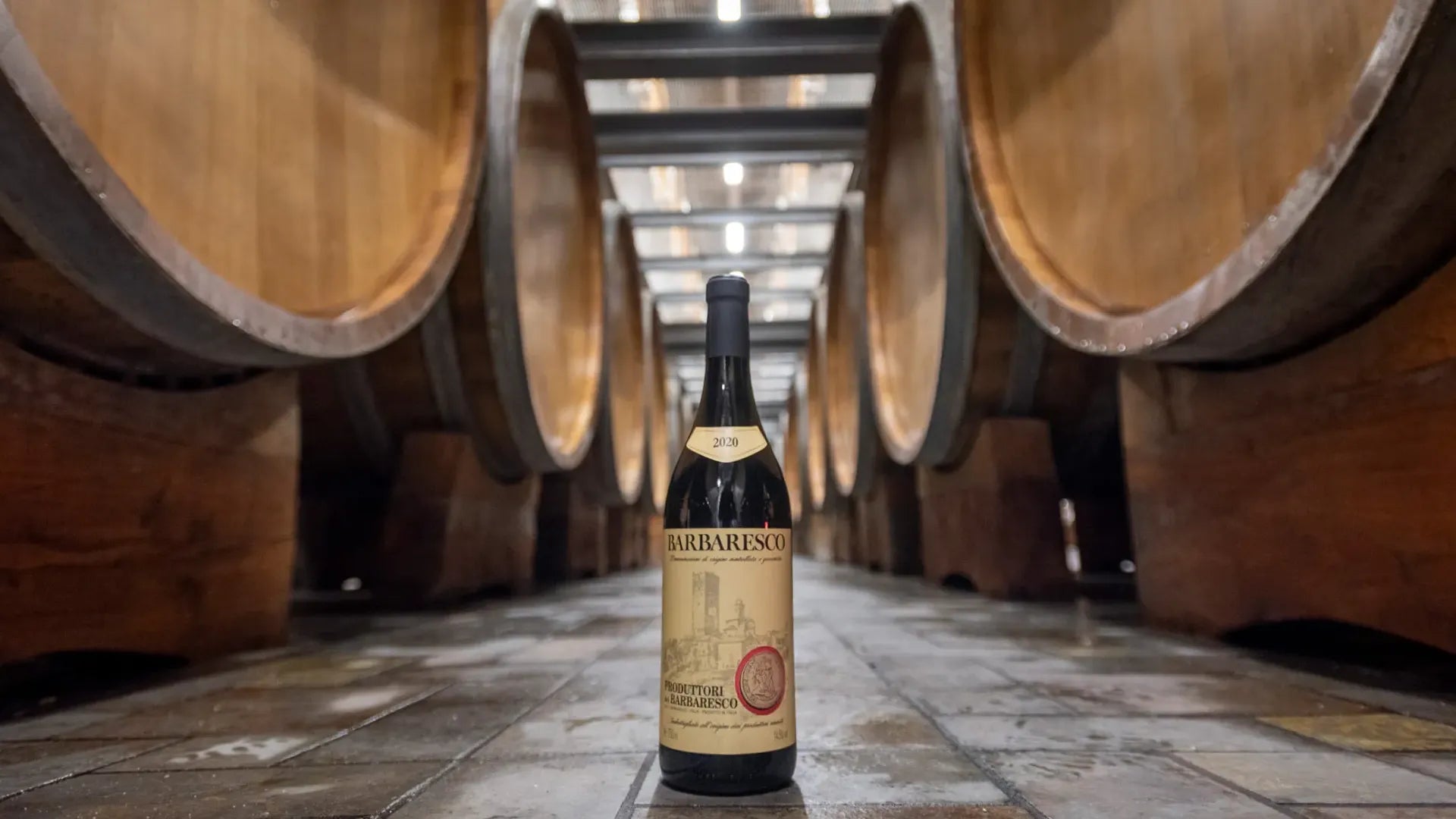 2020 Barbaresco bottle from Produttori del Barbaresco placed in the winery’s cellar among large oak barrels.
