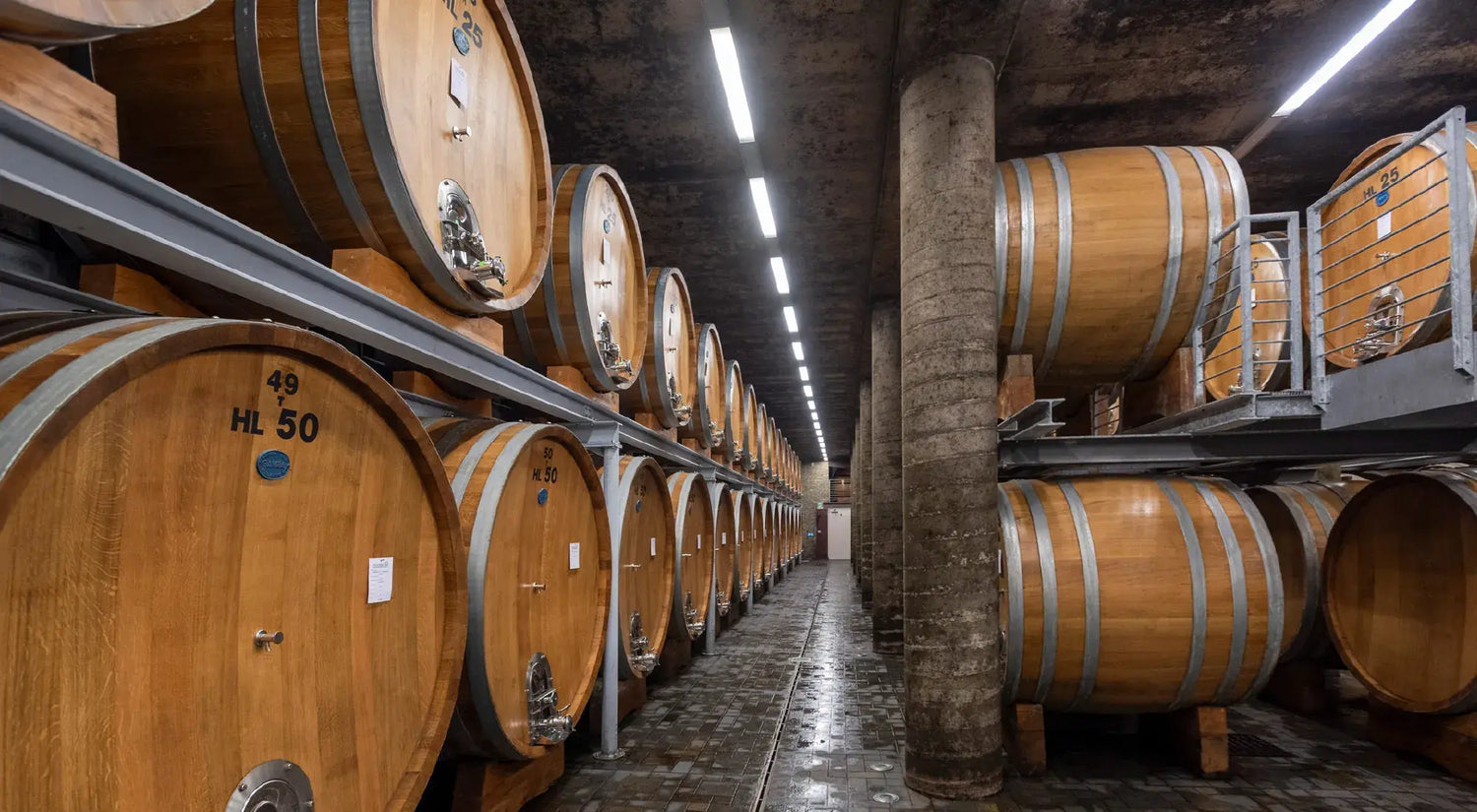 Wooden wine barrels in the Produttori del Barbaresco cellar, neatly stacked along a stone‑tiled corridor.
